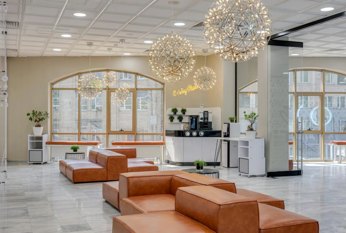 Café-lounge d'un coworking premium : canapés en cuir, luminaires design suspendus, bar barista et espace de convivialité communautaire